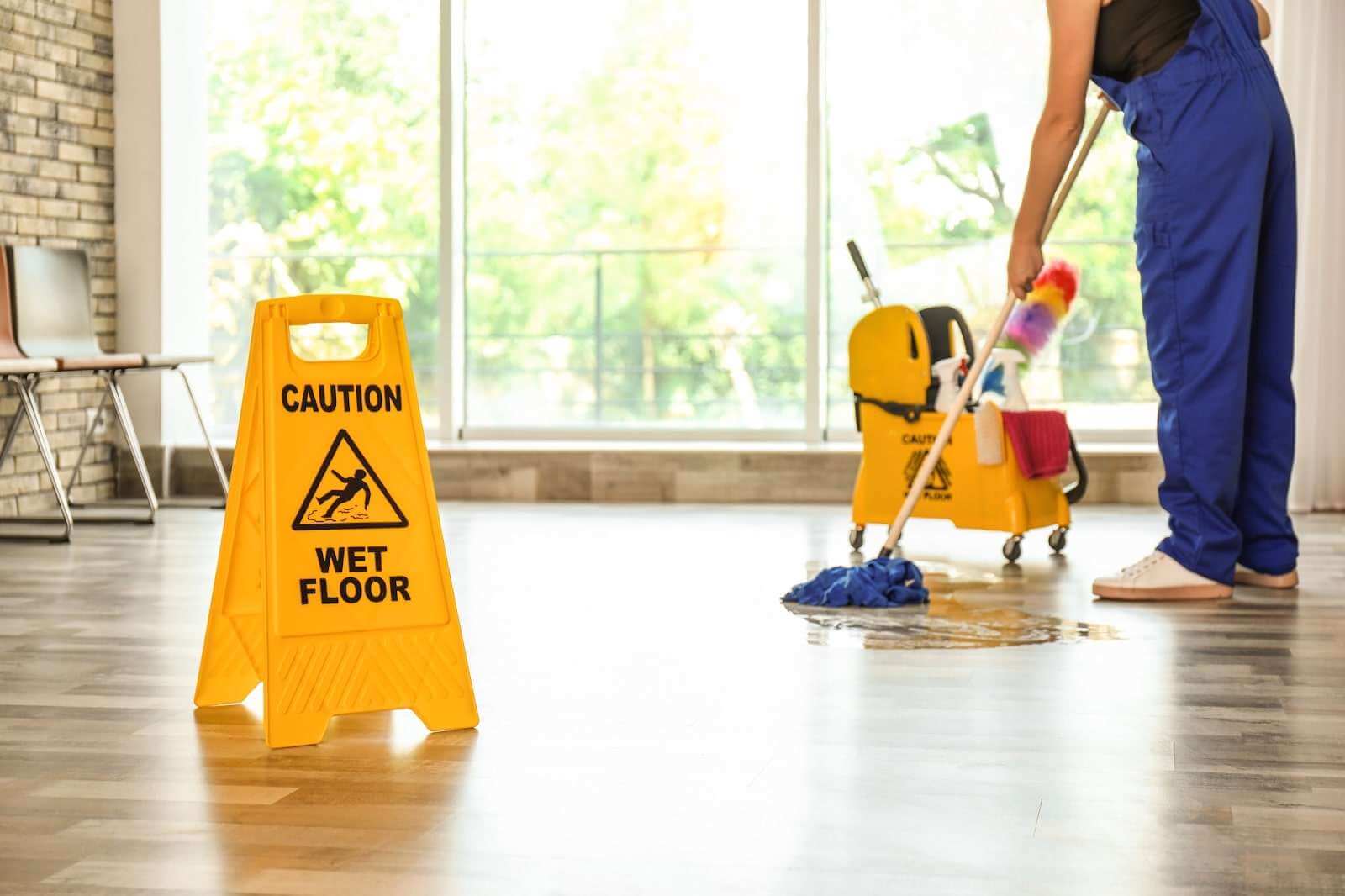 Yellow caution wet floor sign on a wooden floor with a person mopping nearby.