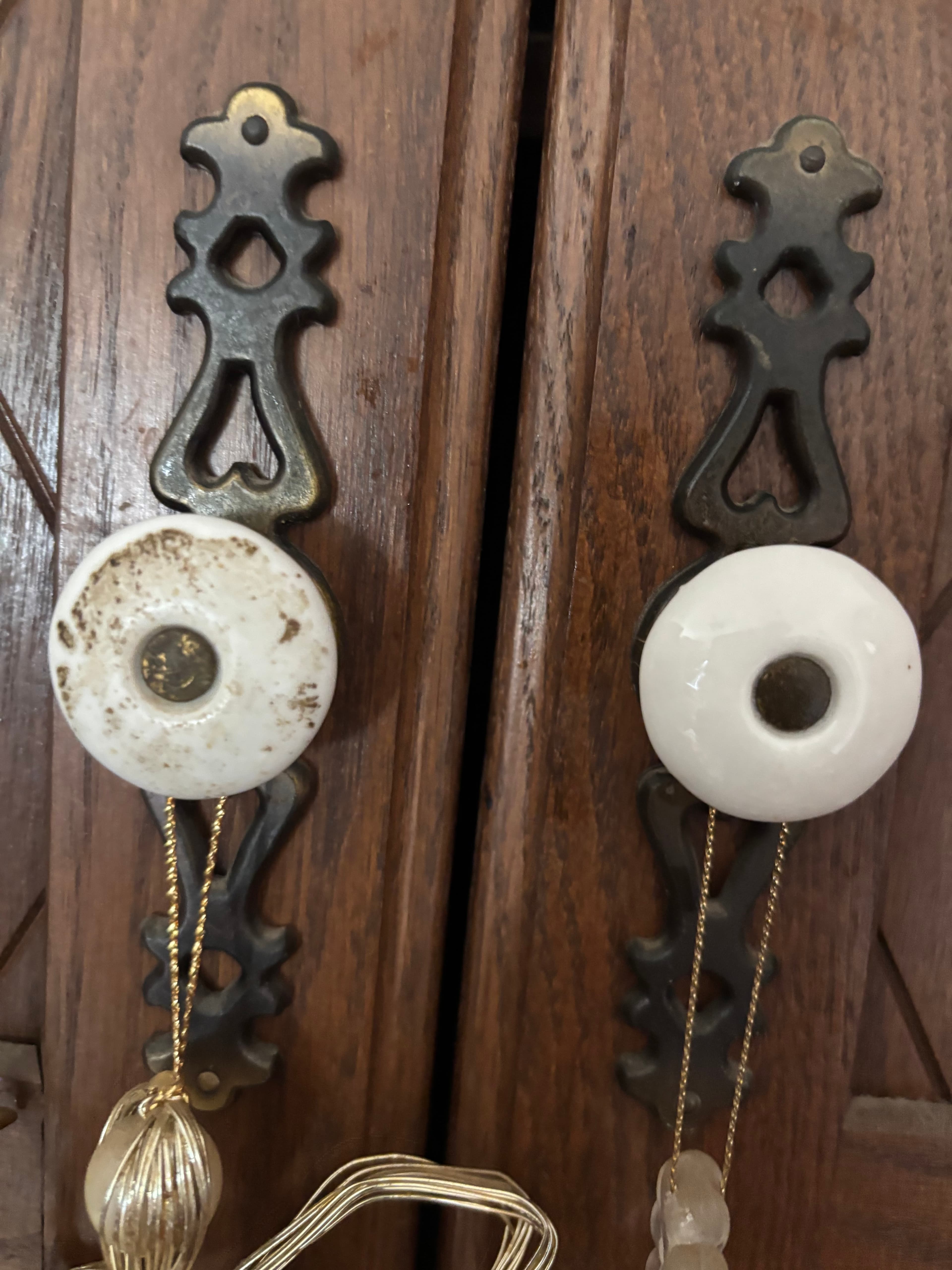 Two white ceramic knobs on ornate metal backplates on wooden doors with hanging gold tassels.