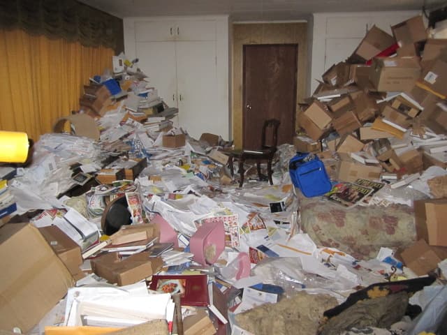 Towering piles of boxes and scattered papers completely fill a room, showing extreme hoarding.
