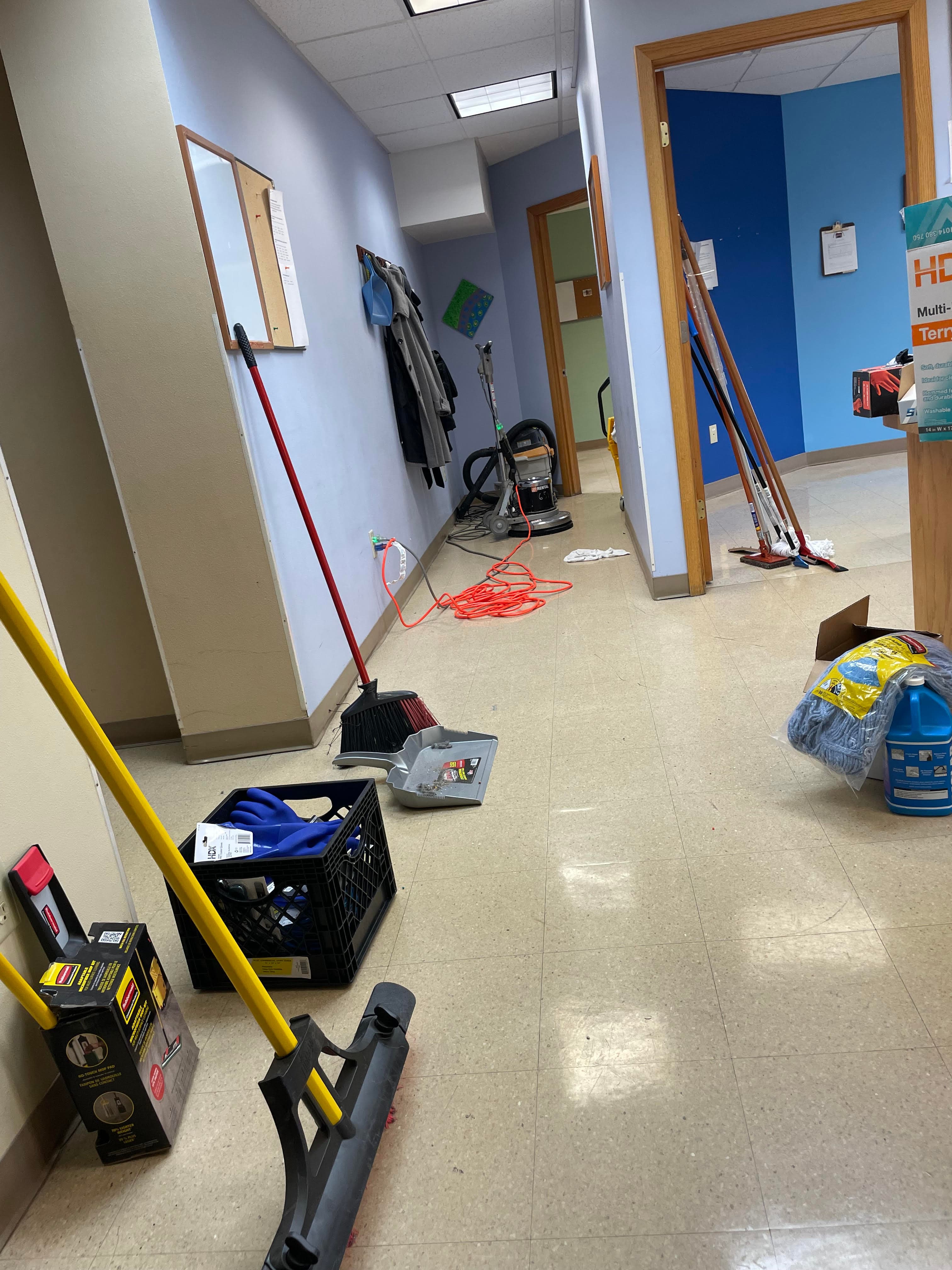 Cleaning supplies including a broom, dustpan, and floor buffer scattered throughout a commercial hallway.